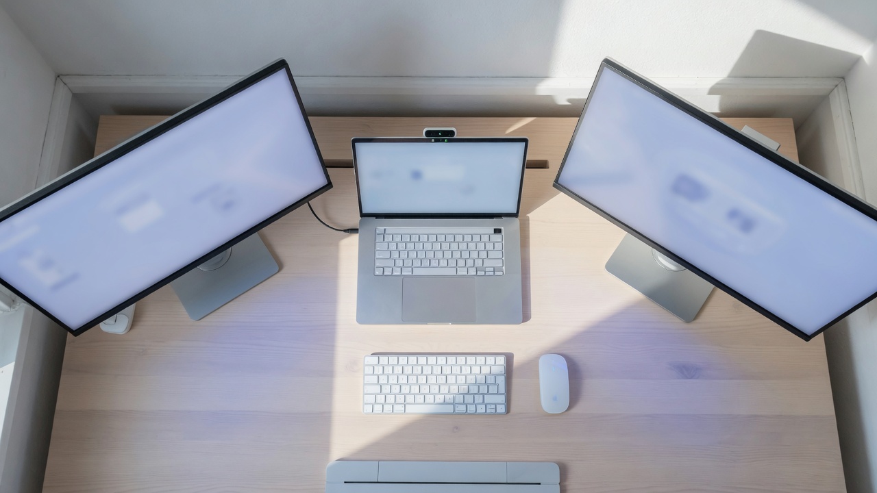 A laptop in the centre of the desk with a monitor on each side.