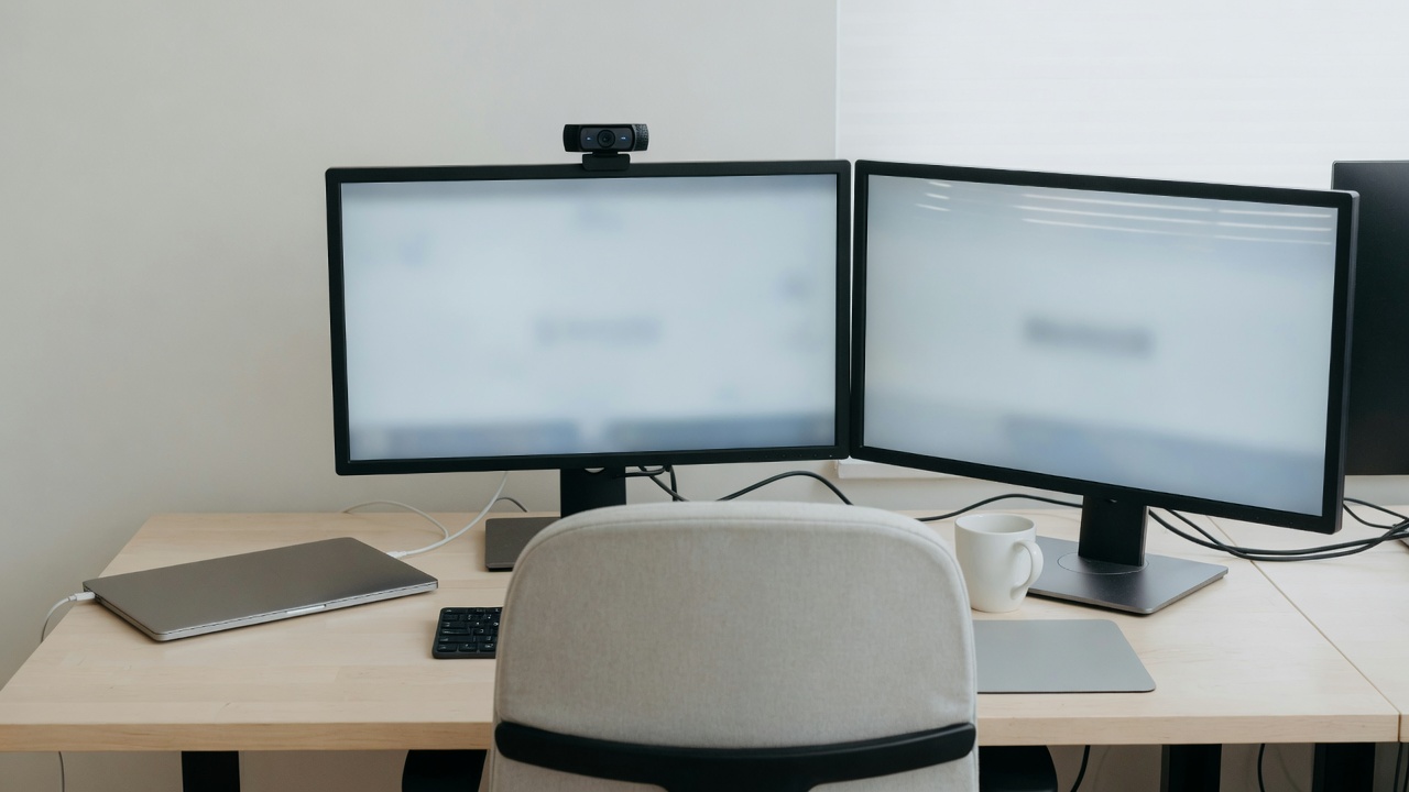 Two monitors in front with an external webcam on top, laptop closed to the side.